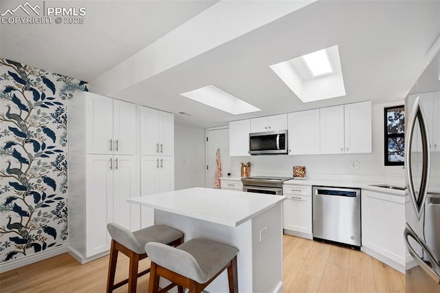 kitchen with appliances with stainless steel finishes, light hardwood / wood-style flooring, a kitchen island, and white cabinets