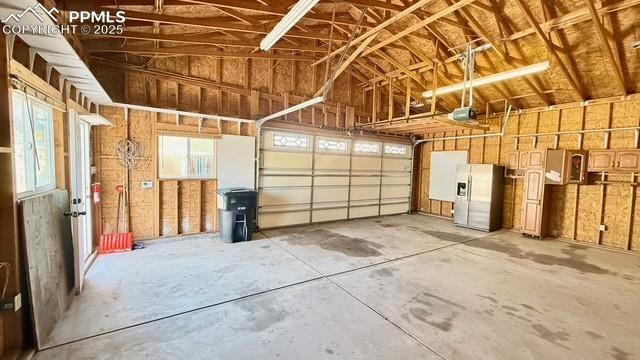 garage with stainless steel fridge with ice dispenser and a garage door opener