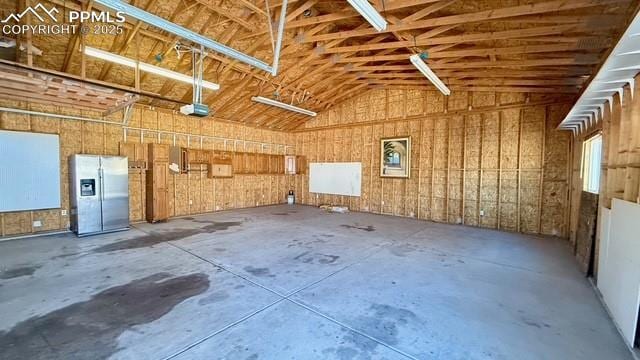 garage with a garage door opener, wood walls, electric panel, and stainless steel fridge