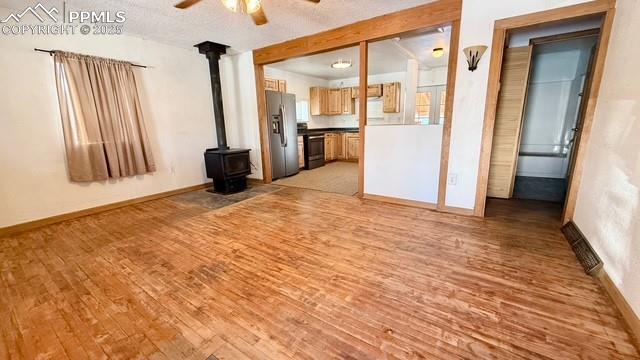 unfurnished living room featuring light hardwood / wood-style floors, a wood stove, a textured ceiling, and ceiling fan