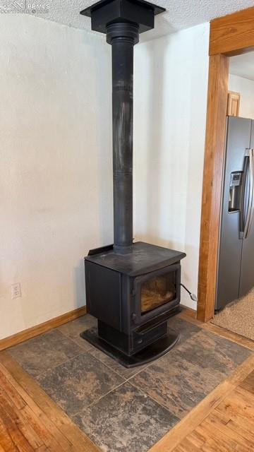 details with stainless steel refrigerator with ice dispenser, a wood stove, a textured ceiling, and hardwood / wood-style floors