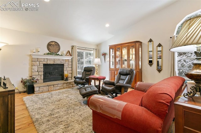 living room featuring lofted ceiling, a stone fireplace, and light wood-type flooring