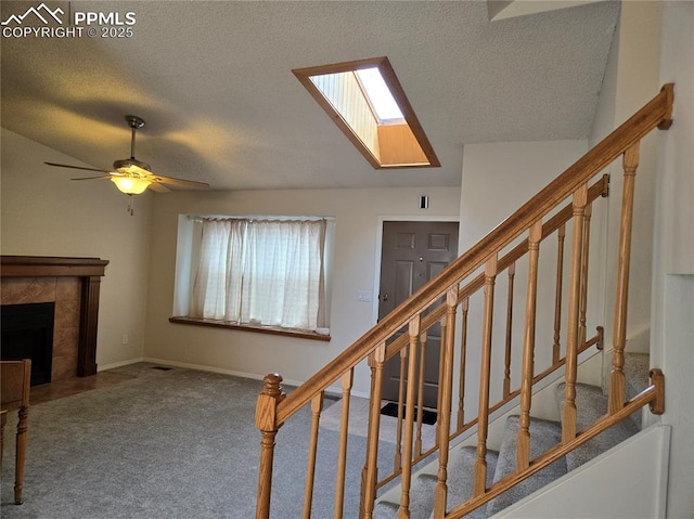 staircase featuring ceiling fan, a tile fireplace, carpet floors, a textured ceiling, and a skylight