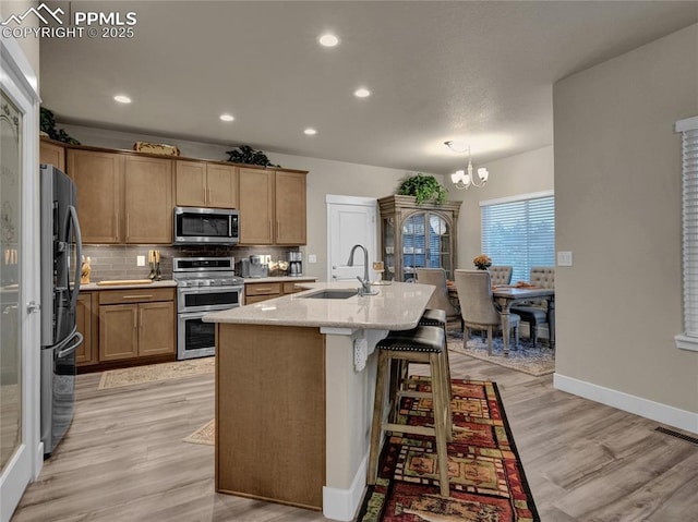 kitchen with appliances with stainless steel finishes, sink, a kitchen island with sink, light hardwood / wood-style floors, and an inviting chandelier