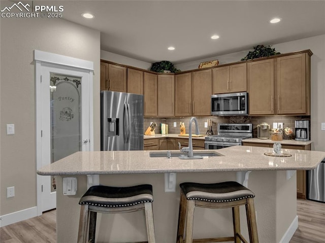 kitchen featuring light hardwood / wood-style floors, appliances with stainless steel finishes, a center island with sink, and tasteful backsplash