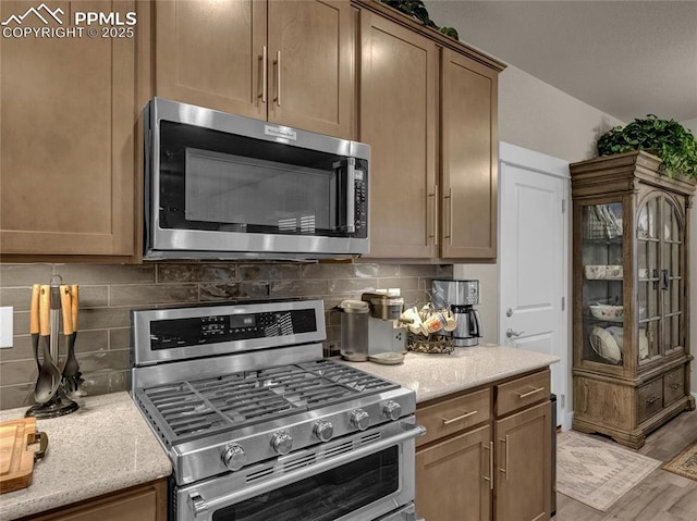 kitchen with backsplash, light hardwood / wood-style flooring, light stone countertops, and appliances with stainless steel finishes