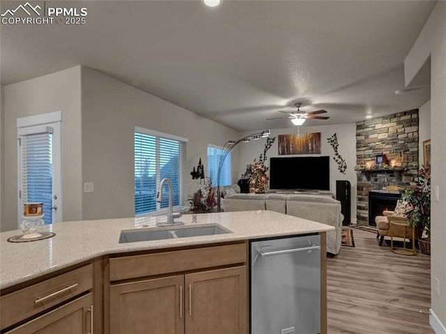 kitchen with dishwasher, a stone fireplace, light hardwood / wood-style floors, sink, and ceiling fan