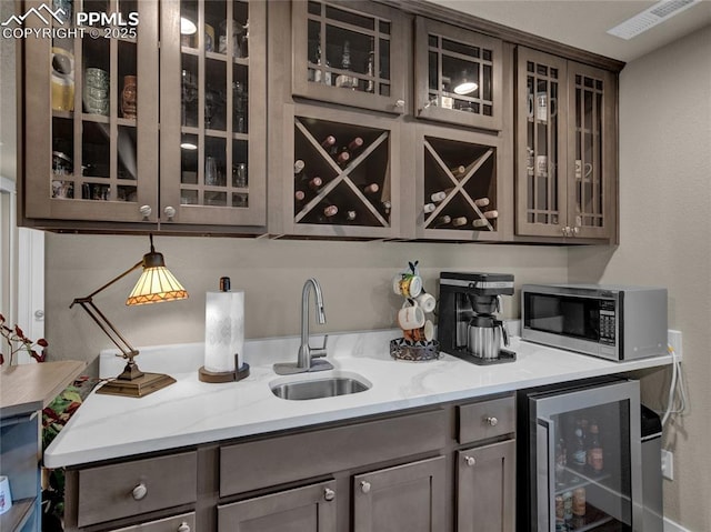 bar featuring light stone countertops, sink, dark brown cabinets, and wine cooler