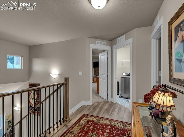 hallway featuring light wood-type flooring, a textured ceiling, and washer / dryer