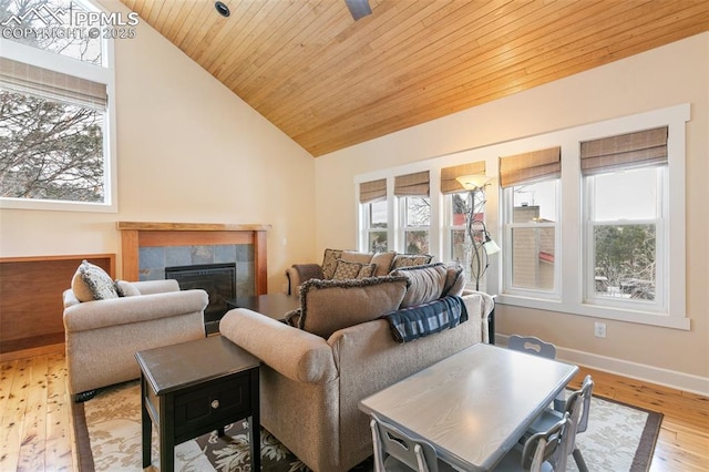 living room featuring vaulted ceiling, a tiled fireplace, light hardwood / wood-style floors, and wooden ceiling