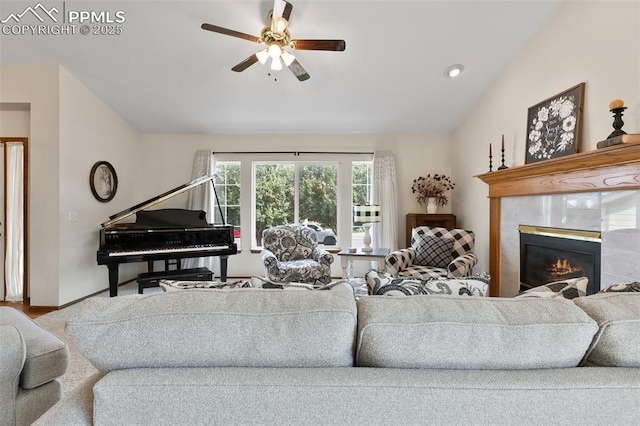 living room with ceiling fan, a tiled fireplace, and lofted ceiling