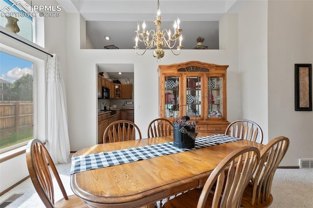 dining area featuring an inviting chandelier, carpet flooring, and a towering ceiling