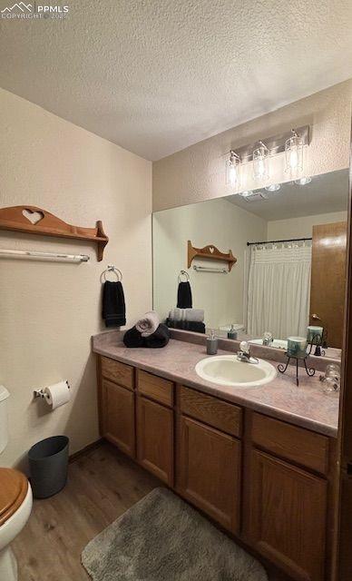 bathroom with a textured ceiling, vanity, toilet, a shower with shower curtain, and hardwood / wood-style flooring