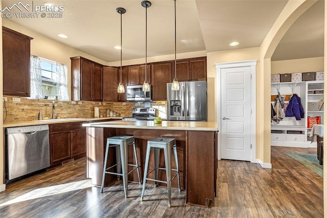 kitchen with sink, dark wood-type flooring, stainless steel appliances, a kitchen island, and decorative light fixtures