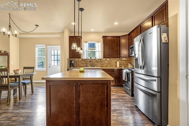 kitchen featuring pendant lighting, dark wood-type flooring, appliances with stainless steel finishes, backsplash, and a center island