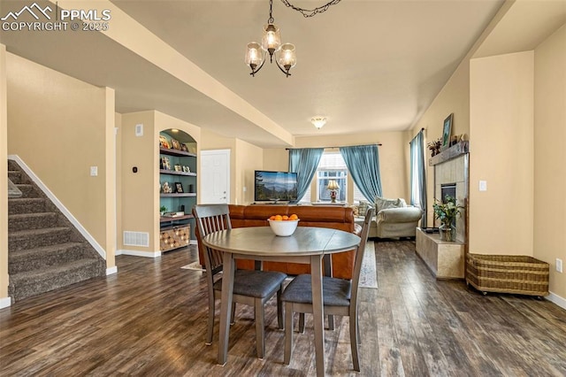 dining area featuring built in features, dark wood-type flooring, a tile fireplace, and a chandelier