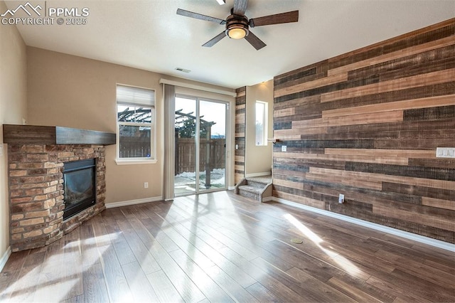 living room featuring ceiling fan, wood-type flooring, a stone fireplace, and wooden walls