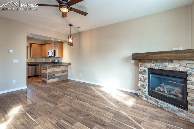 unfurnished living room with a stone fireplace, dark wood-type flooring, and ceiling fan