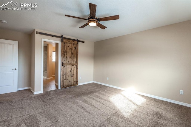 unfurnished bedroom featuring ceiling fan, ensuite bathroom, light carpet, and a barn door