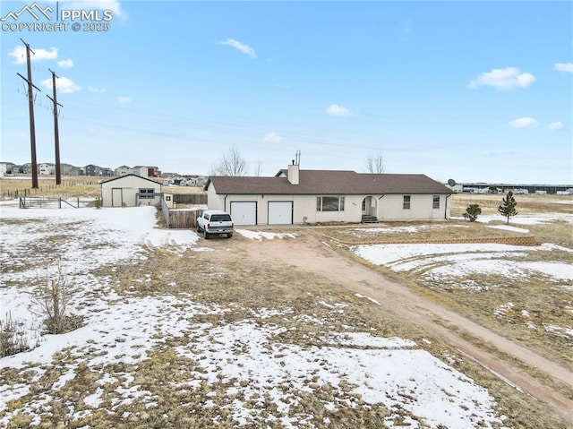 snow covered rear of property with a garage and a storage unit