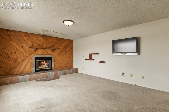 unfurnished living room featuring a tile fireplace, carpet flooring, track lighting, a textured ceiling, and wood walls