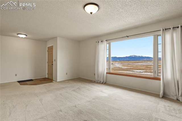 spare room featuring a mountain view, carpet floors, and a textured ceiling
