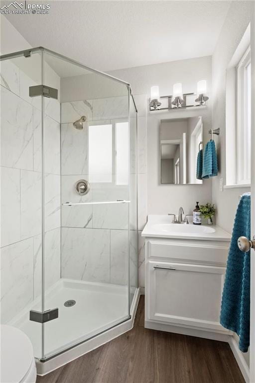 bathroom featuring hardwood / wood-style flooring, vanity, a shower with door, and toilet