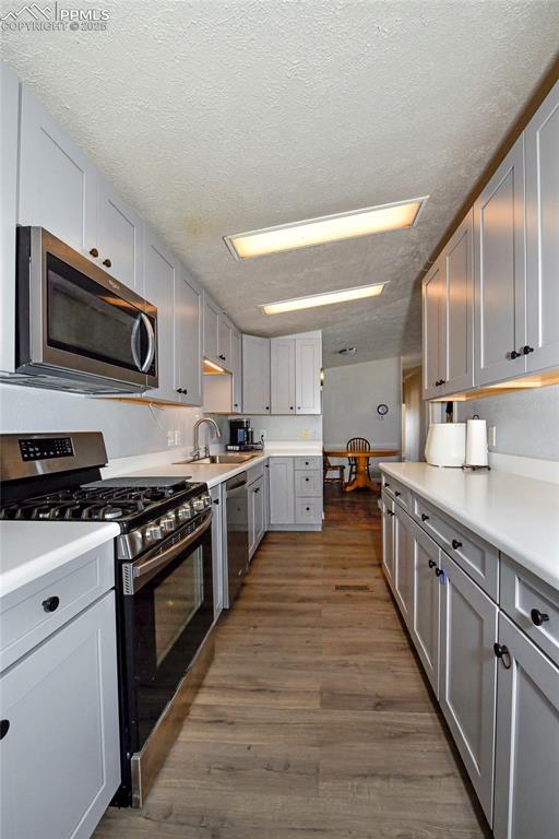 kitchen featuring dark wood-type flooring, sink, gray cabinetry, a textured ceiling, and appliances with stainless steel finishes