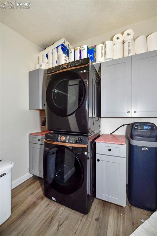 laundry area with cabinets, stacked washer / dryer, and hardwood / wood-style floors