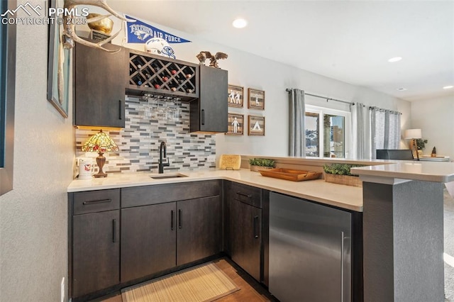 kitchen featuring sink, decorative backsplash, fridge, kitchen peninsula, and dark brown cabinets