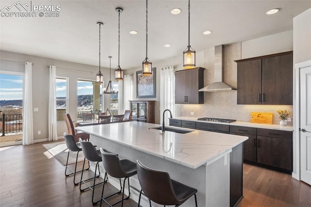 kitchen featuring wall chimney exhaust hood, a kitchen island with sink, sink, and dark brown cabinets