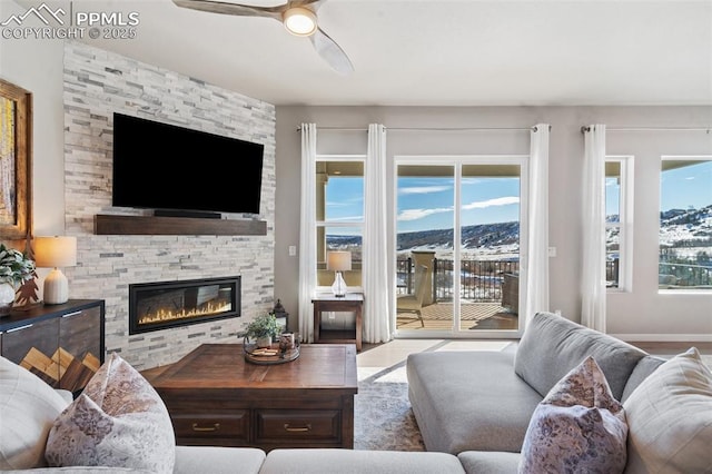 living room with a fireplace, a wealth of natural light, a mountain view, and ceiling fan