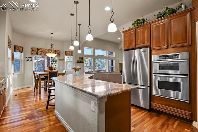 kitchen featuring a center island, appliances with stainless steel finishes, decorative light fixtures, a breakfast bar, and light stone counters