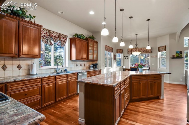 kitchen featuring a center island, sink, hanging light fixtures, light wood-type flooring, and light stone counters