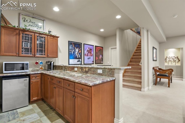 kitchen featuring light colored carpet, kitchen peninsula, light stone countertops, and stainless steel fridge