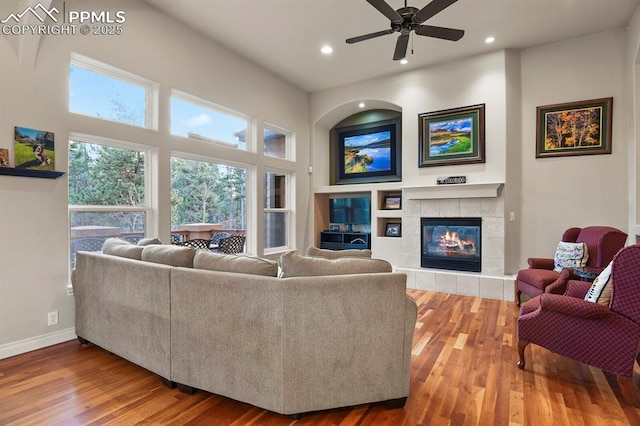 living room featuring ceiling fan, a tiled fireplace, and wood-type flooring