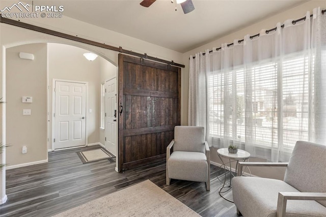 sitting room with ceiling fan, dark wood-type flooring, and a barn door