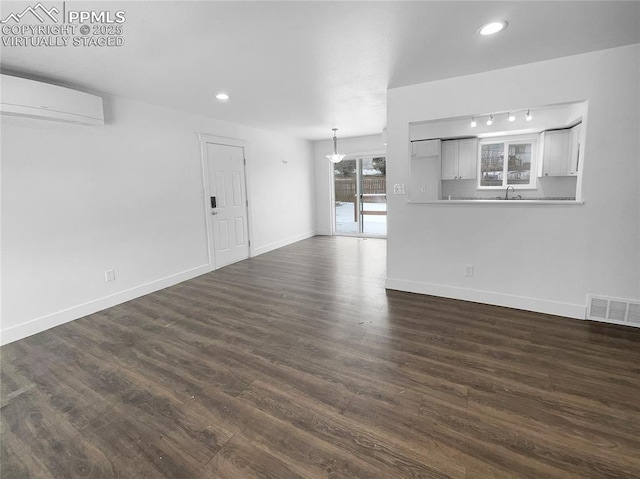 unfurnished living room with sink, dark hardwood / wood-style flooring, a wall unit AC, and track lighting