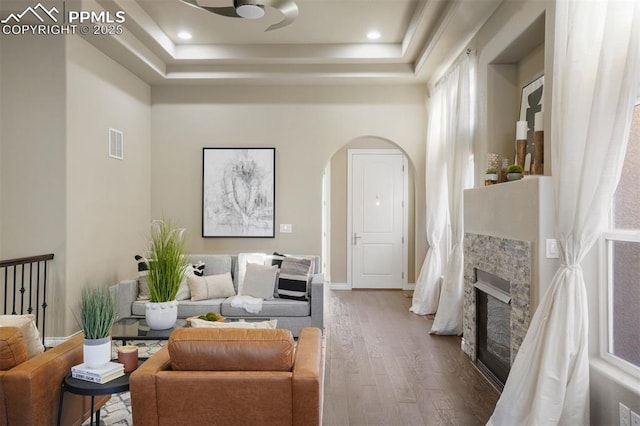 living room with hardwood / wood-style flooring, a raised ceiling, and a stone fireplace