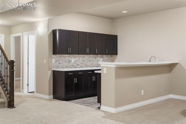 kitchen with dark brown cabinets, backsplash, kitchen peninsula, and light carpet