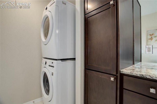 clothes washing area featuring stacked washer and clothes dryer, cabinet space, and baseboards