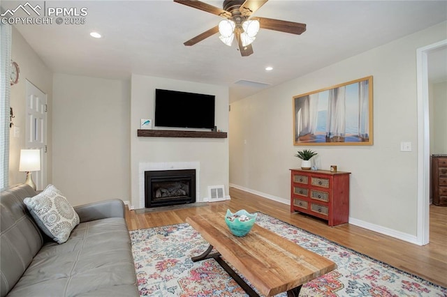 living room featuring baseboards, visible vents, wood finished floors, and a fireplace with flush hearth