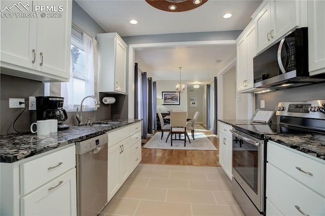 kitchen featuring white cabinets, dark stone countertops, stainless steel appliances, and a sink