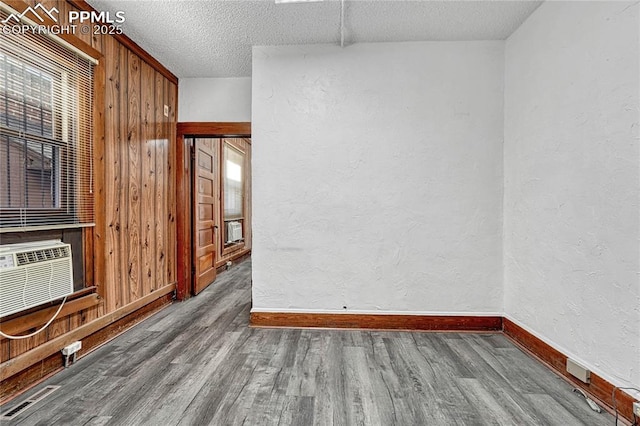 spare room with cooling unit, wood-type flooring, a textured ceiling, and wood walls