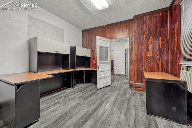 office area with built in desk, light hardwood / wood-style floors, a textured ceiling, and wood walls