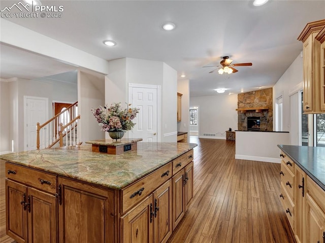 kitchen with a center island, a stone fireplace, ceiling fan, light stone counters, and light hardwood / wood-style flooring