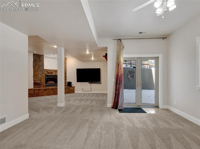 unfurnished living room with french doors, a stone fireplace, ceiling fan, and light colored carpet