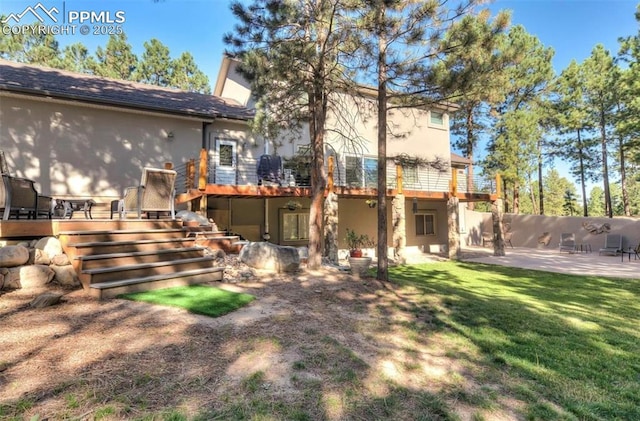 rear view of property featuring a wooden deck, a lawn, and a patio