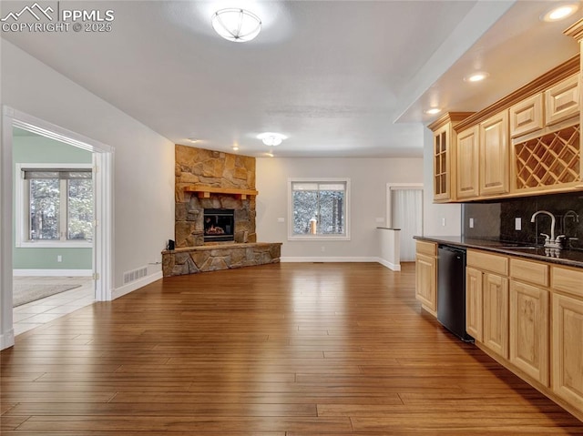 kitchen featuring light brown cabinets, black dishwasher, a stone fireplace, tasteful backsplash, and sink