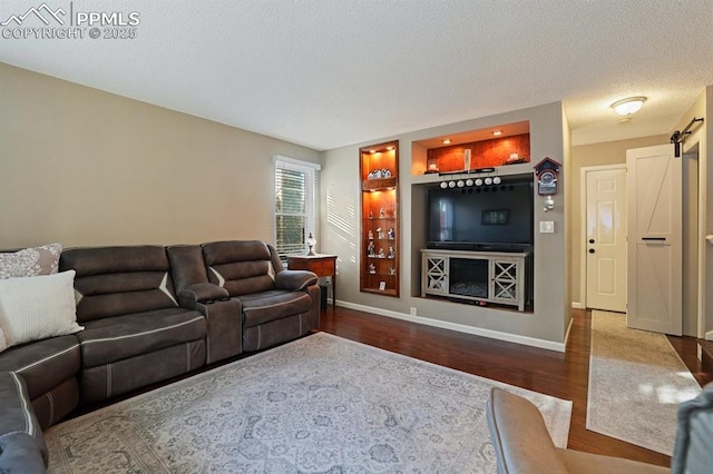 living room featuring hardwood / wood-style flooring, a barn door, built in features, and a textured ceiling